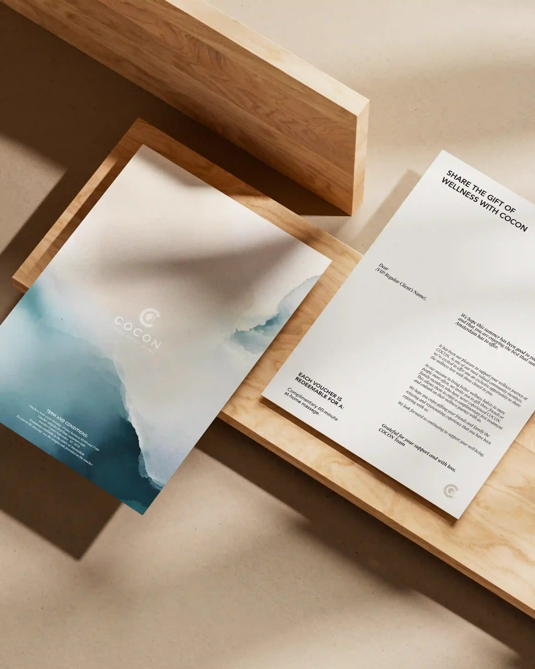 COCON wellness gift voucher and branded stationery featuring blue watercolour designs, arranged on natural wooden surfaces.